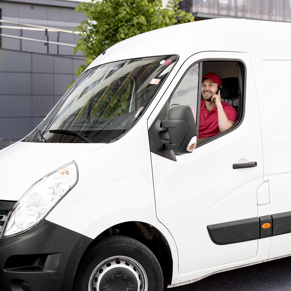 A man with a red shirt and hat in a service vehicle on his phone